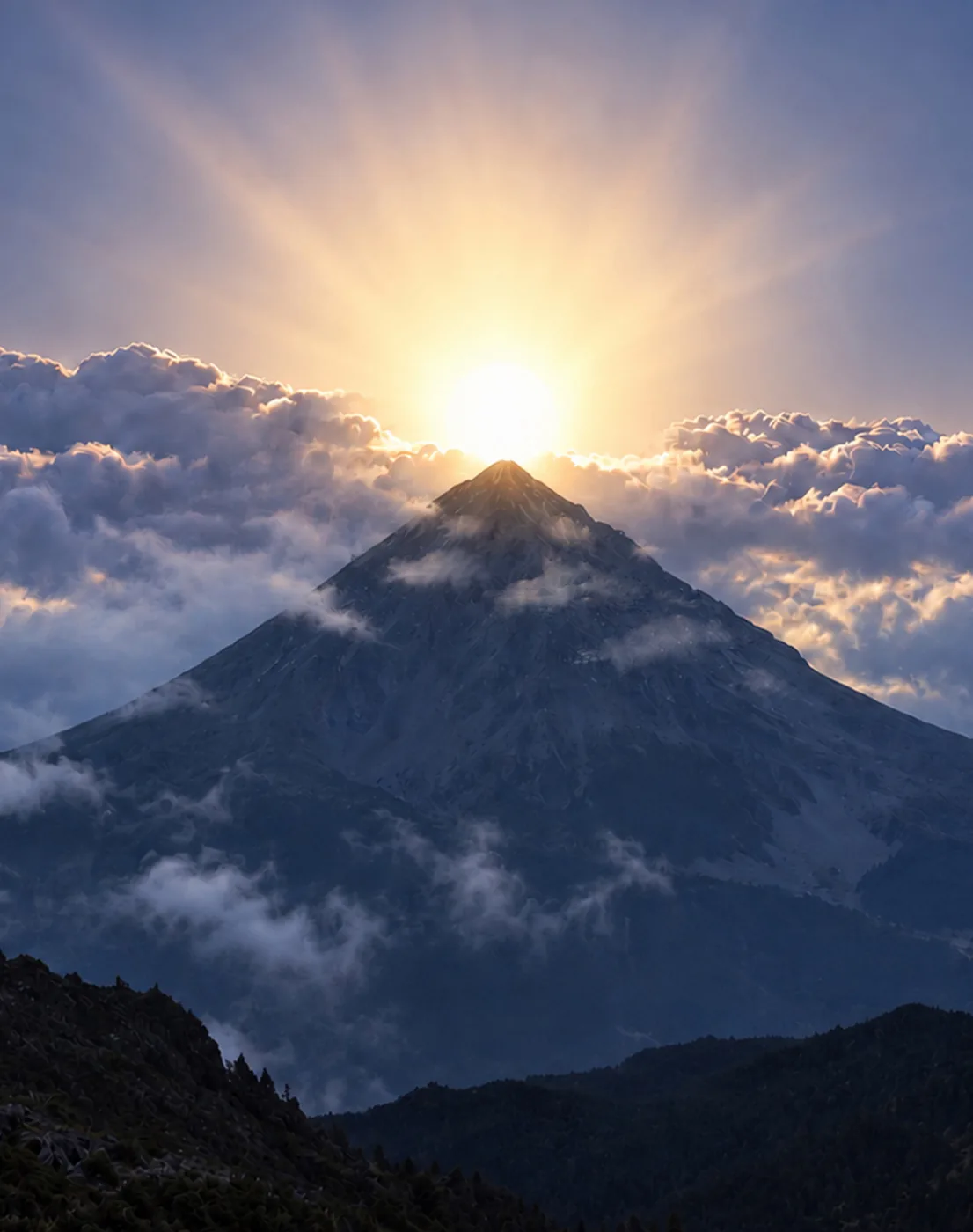 The sun bursting over the peak of a volcano above a sea of clouds