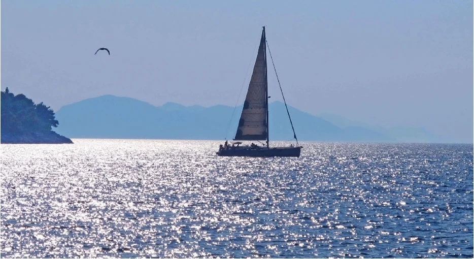 A white sailboat crossing calm water beneath a broad sky